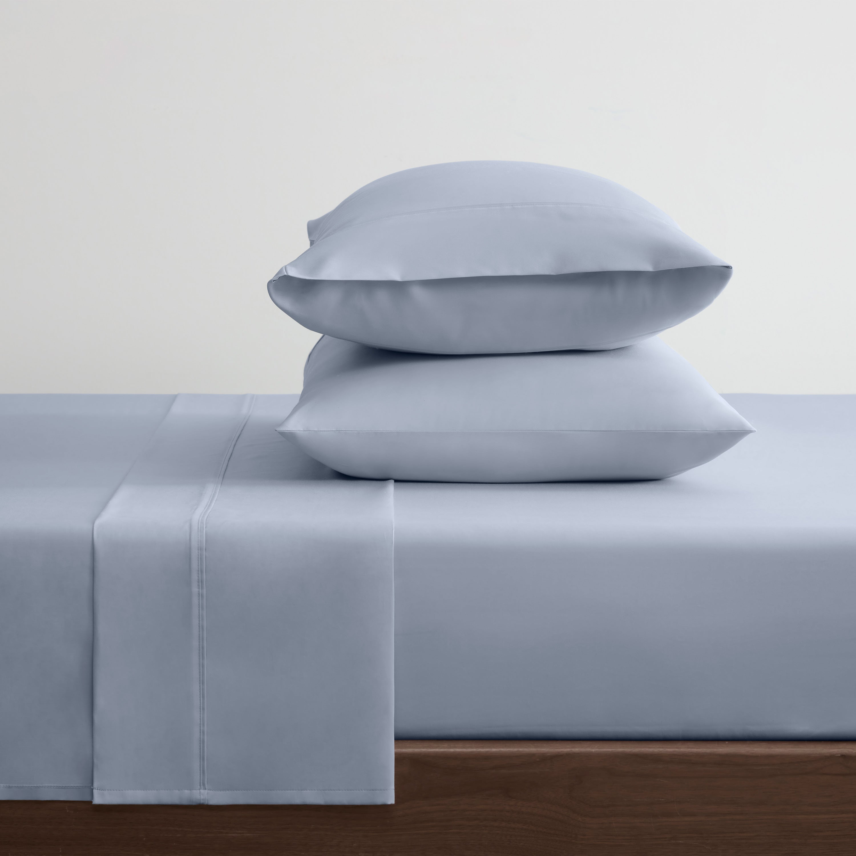 Solid light blue cotton and Tencel sheet set with two stacked pillows on a bed.