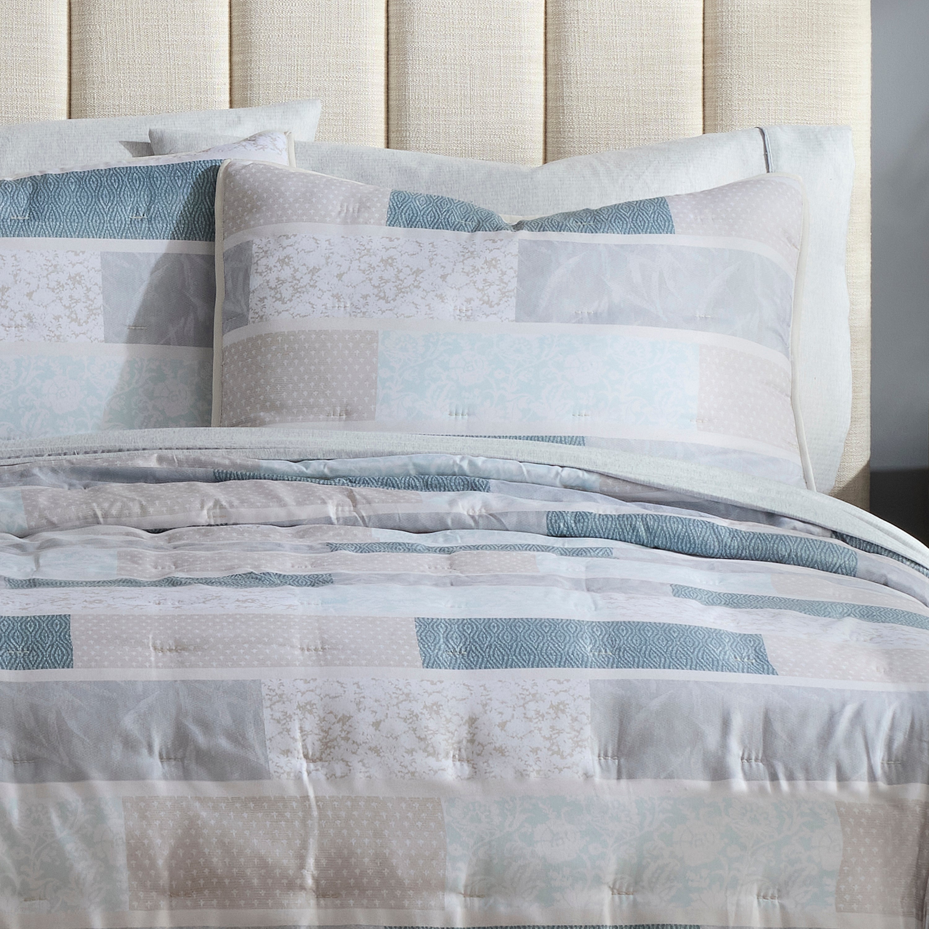 Quilt set featuring a patchwork design in soft blue and neutral tones with matching decorative pillows.