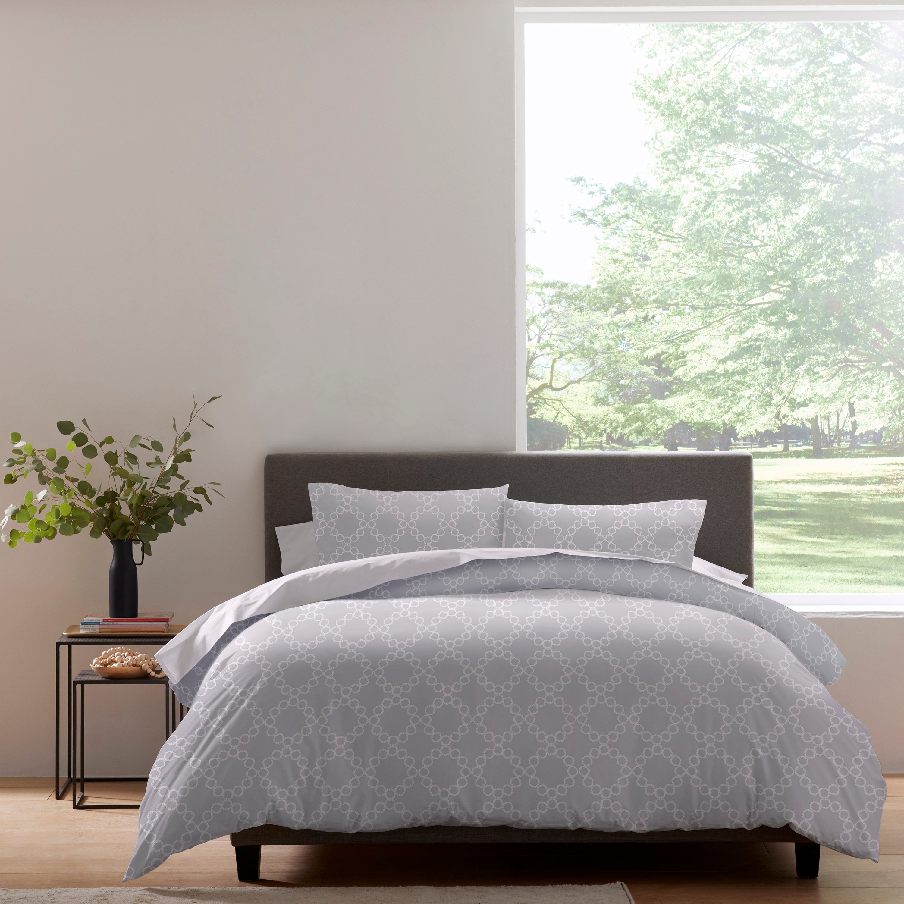 Duvet set featuring a geometric pattern in light gray, displayed on a bed with matching pillows and a plant nearby.