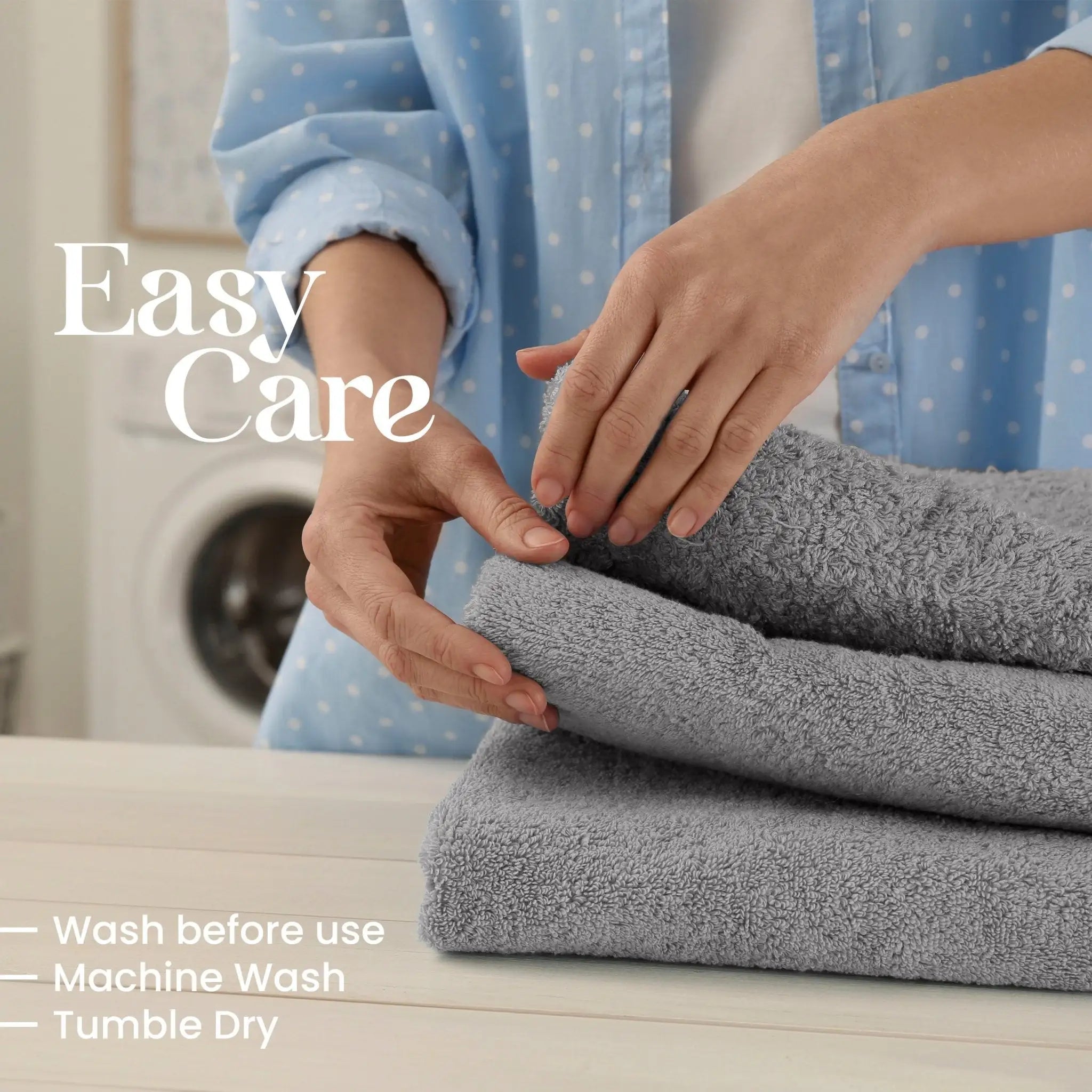 A person folds a gray towel on a light wooden table, with text overlays reading 'Easy Care' and care instructions: 'Wash before use, Machine Wash, Tumble Dry'. A blurred washing machine is visible in the background.