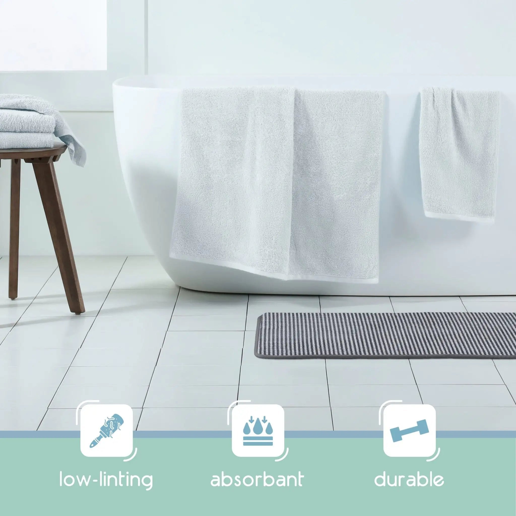 A black bath rug on the floor and three feature icons below reading low-linting, absorbent, and durable.
