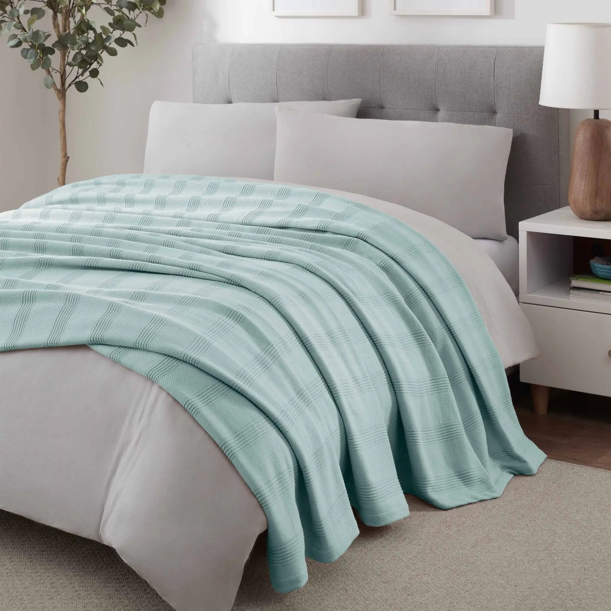 Bed with a light blue blanket and gray headboard in a bedroom setting.