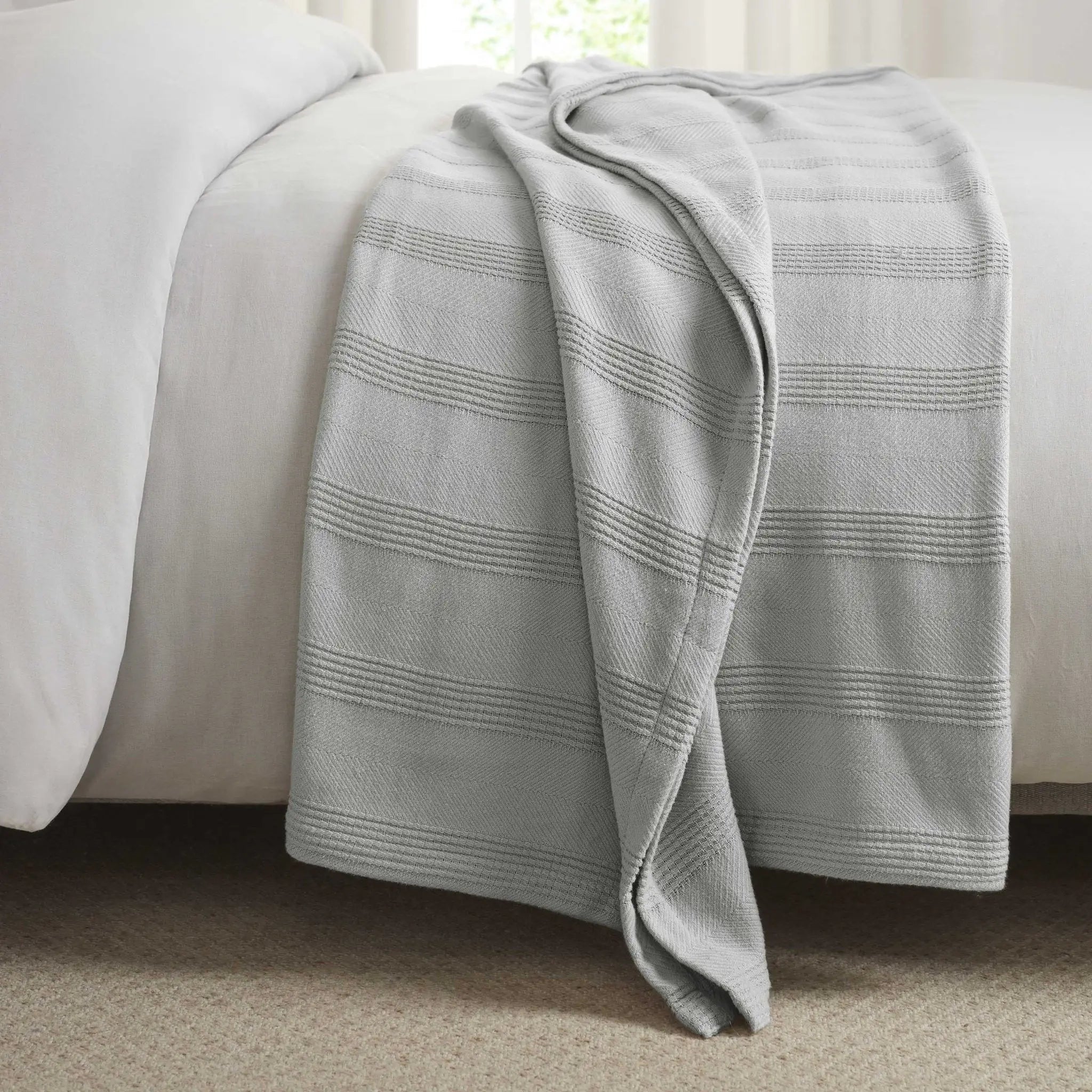 Gray striped blanket draped over a white bed