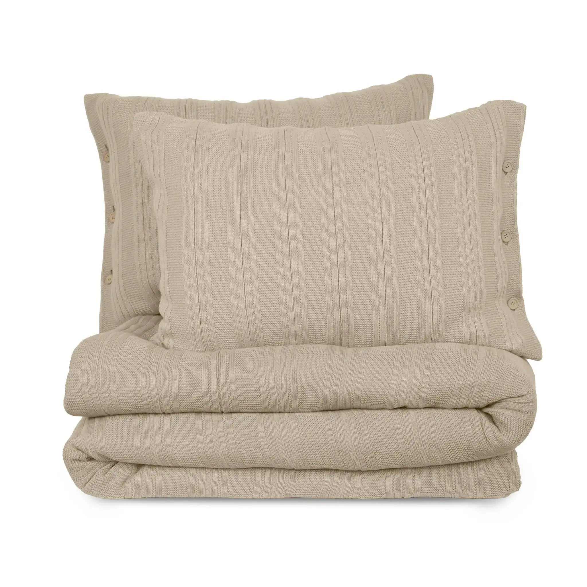 A folded bedding set in a warm beige color, featuring a textured vertical ribbed quilt and two matching pillow shams with decorative side buttons, set against a plain white background.