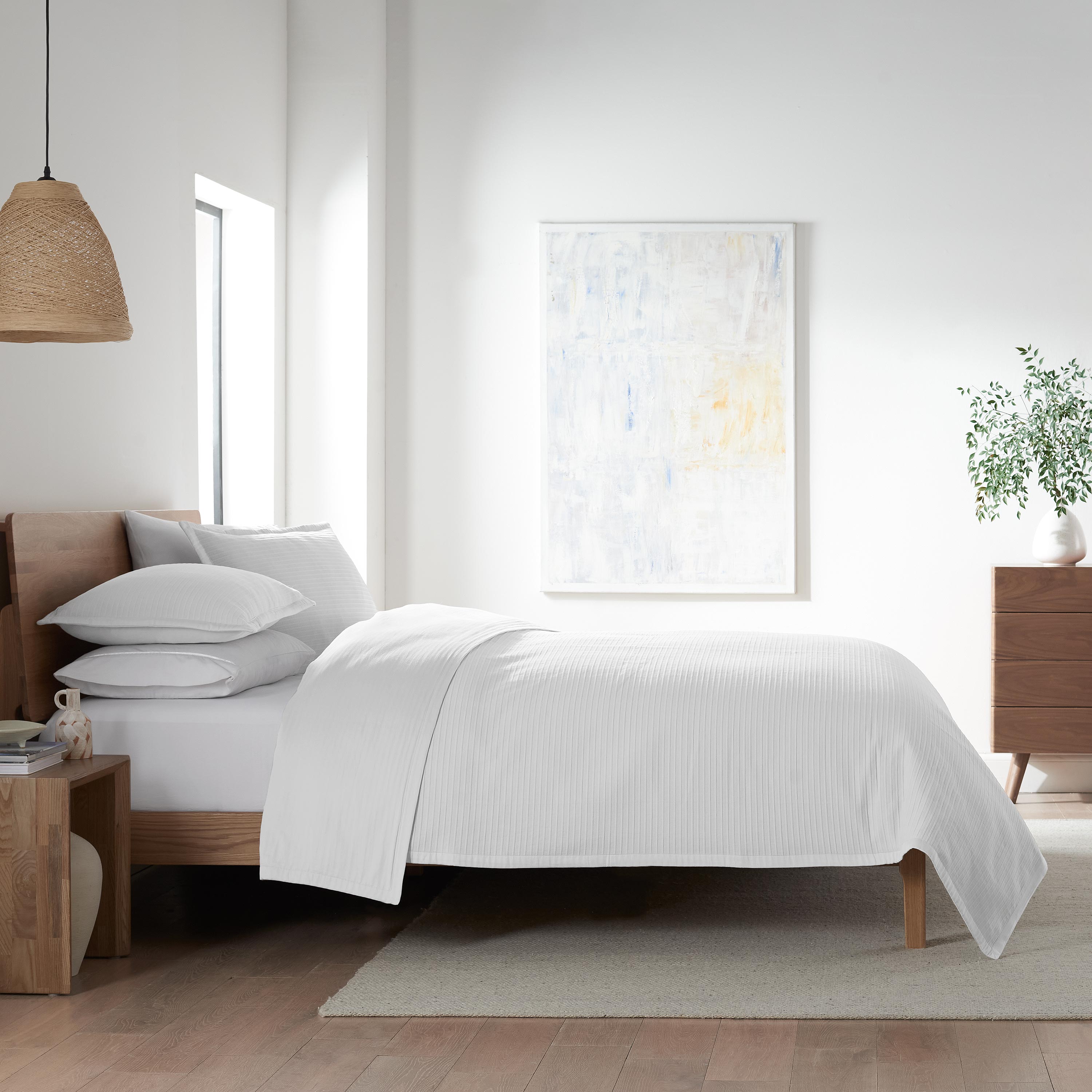 White coverlet set draped over a bed with decorative pillows, wooden furniture, and a minimalist room design.