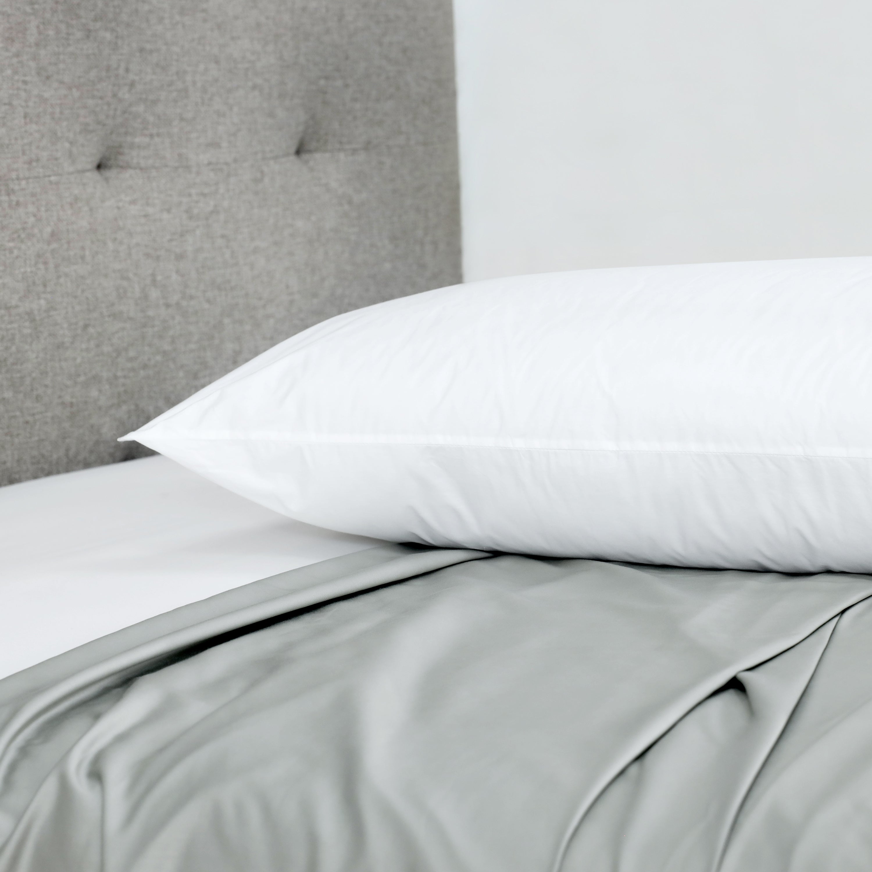 White gusset pillow resting on a bed with gray bedding and a textured gray headboard in the background.