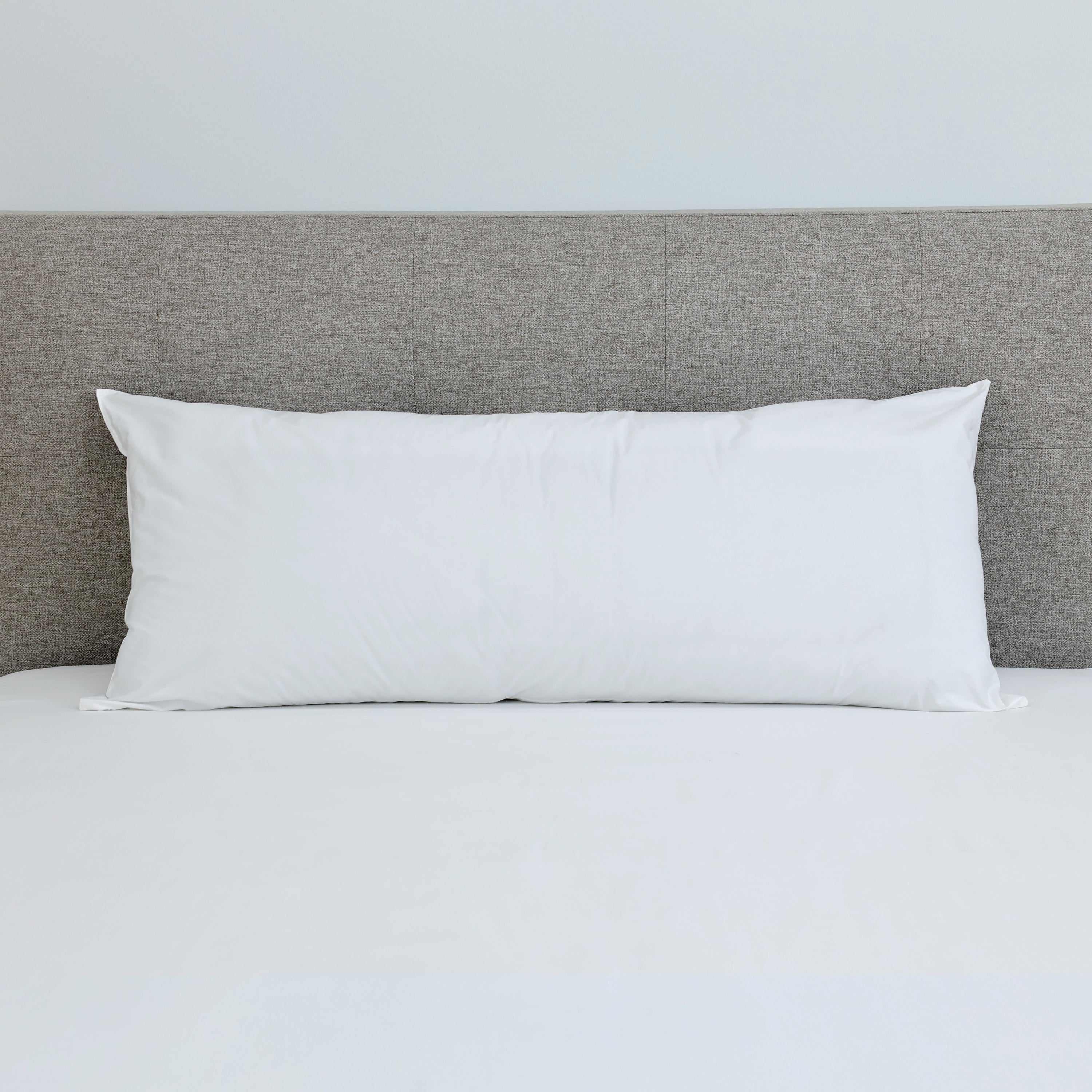 White gusset pillow placed on a bed with a light gray headboard and white bedding.