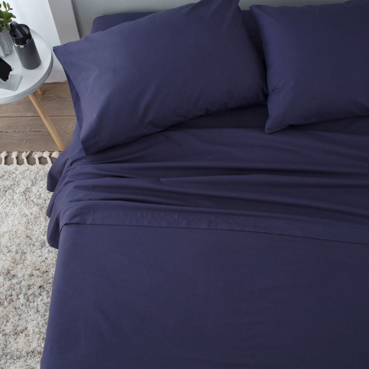 Navy blue sheet set with two pillows on a bed, featuring a smooth, flat surface and a textured rug below.