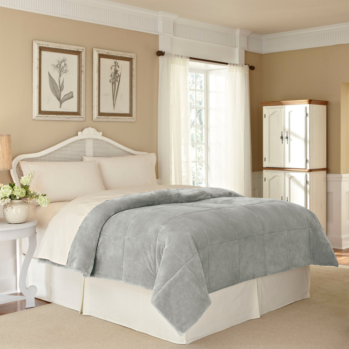 Gray plush blanket draped over a bed with cream-colored bedding in a softly lit bedroom.