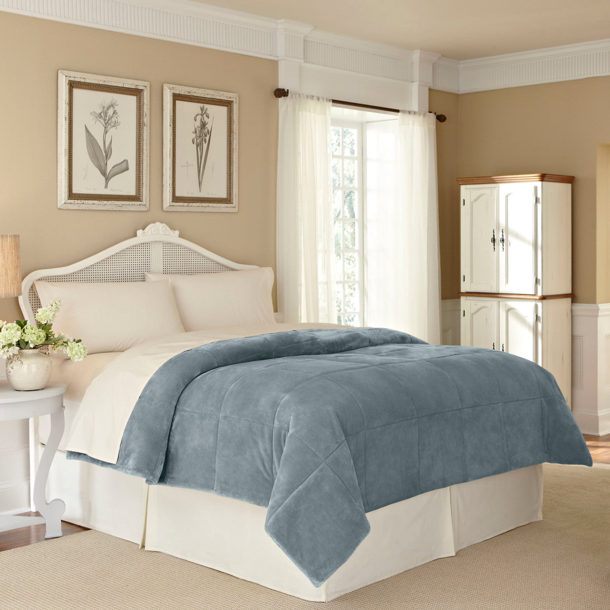 Gray plush blanket draped over a bed with cream-colored bedding in a softly lit room.