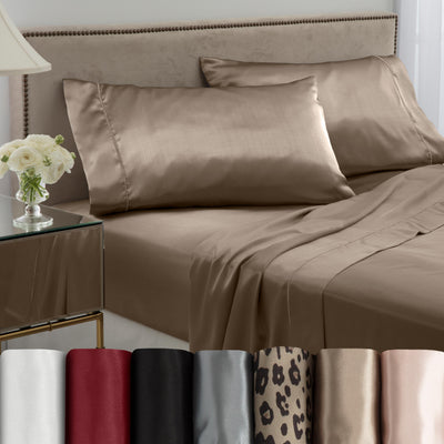 Satin sheet set in various colors displayed on a bed with matching pillows and a bedside table with flowers.