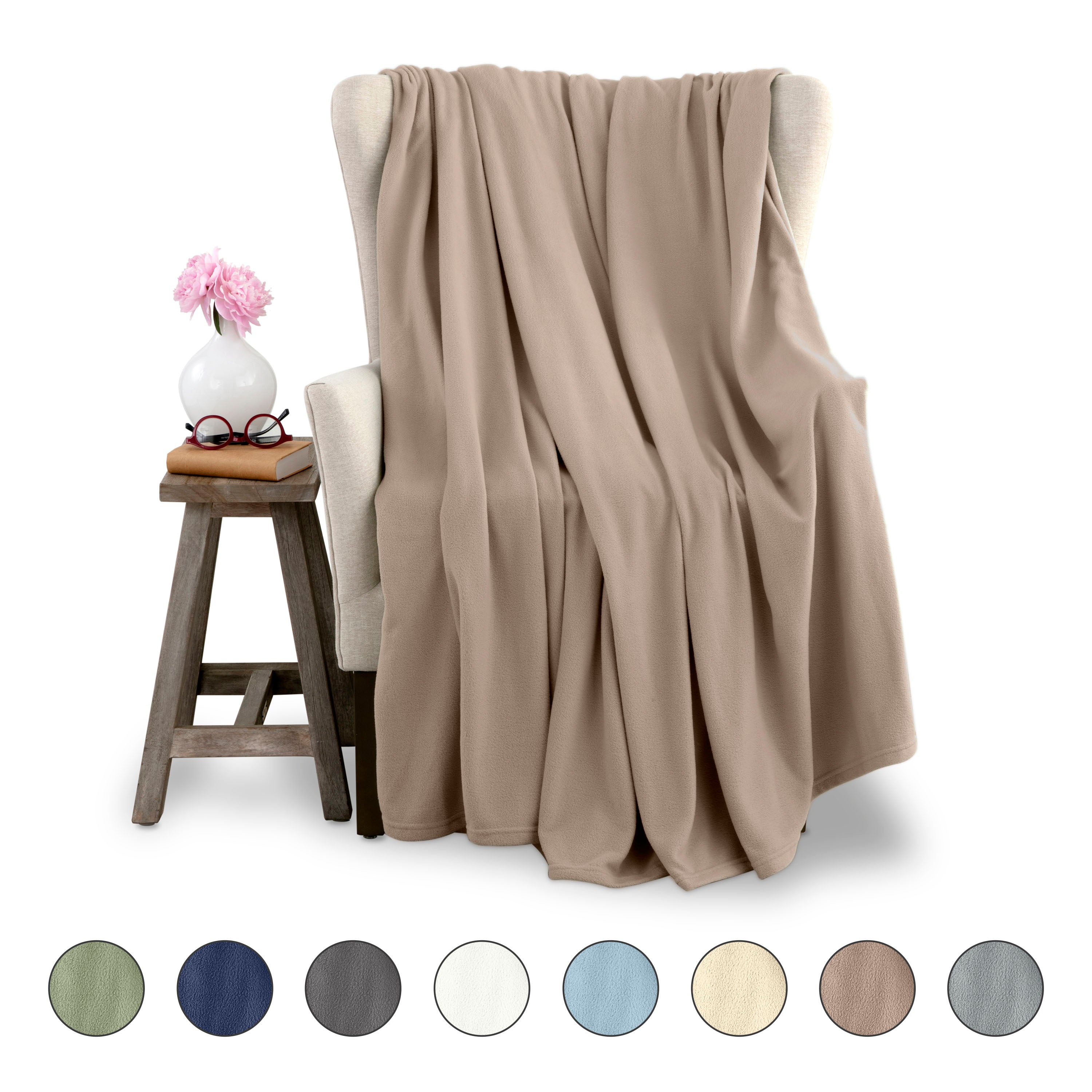 Microfleece blanket draped over a chair next to a small table with a vase and glasses, featuring color swatches below.
