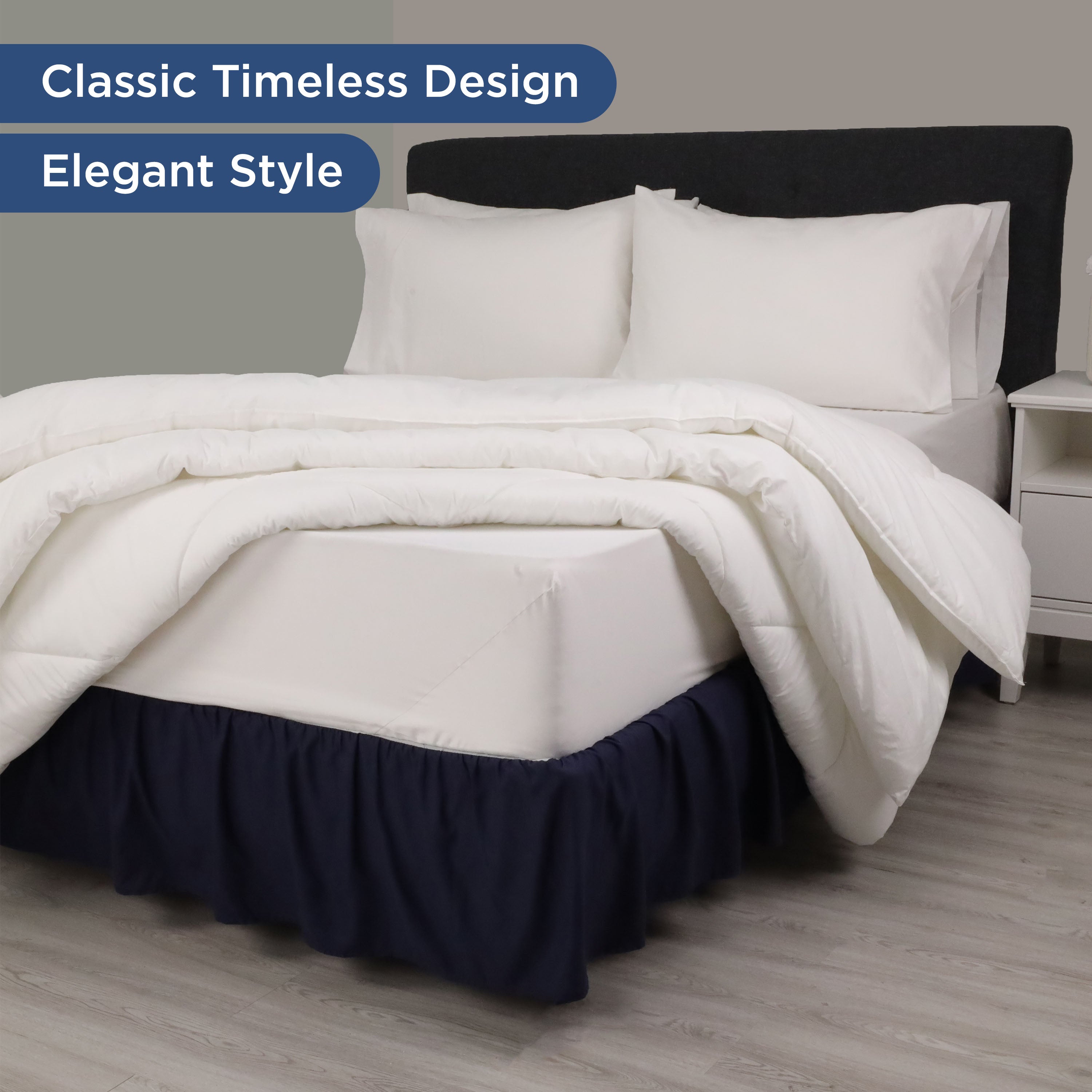Navy ruffle bed skirt drapes over a white mattress, complemented by white bedding and pillows against a gray wall.
