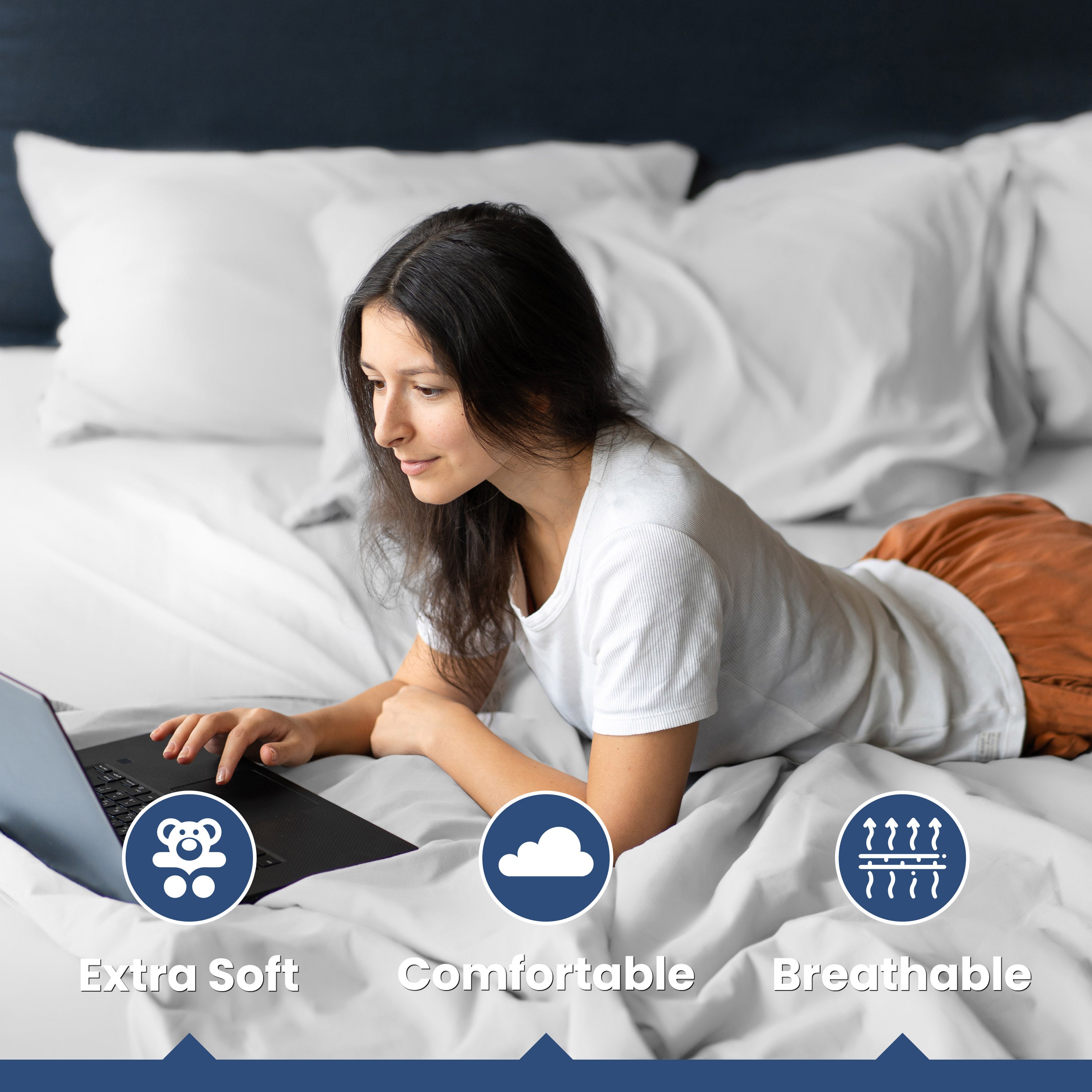 A person is lying on a bed with white sheets and pillows, using a laptop.