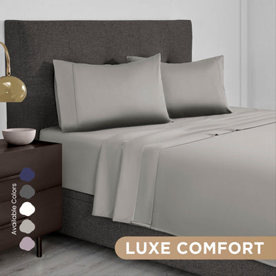 Gray Supima cotton sheet set on a bed with matching pillows and a bedside table featuring a lamp and decorative bowl.