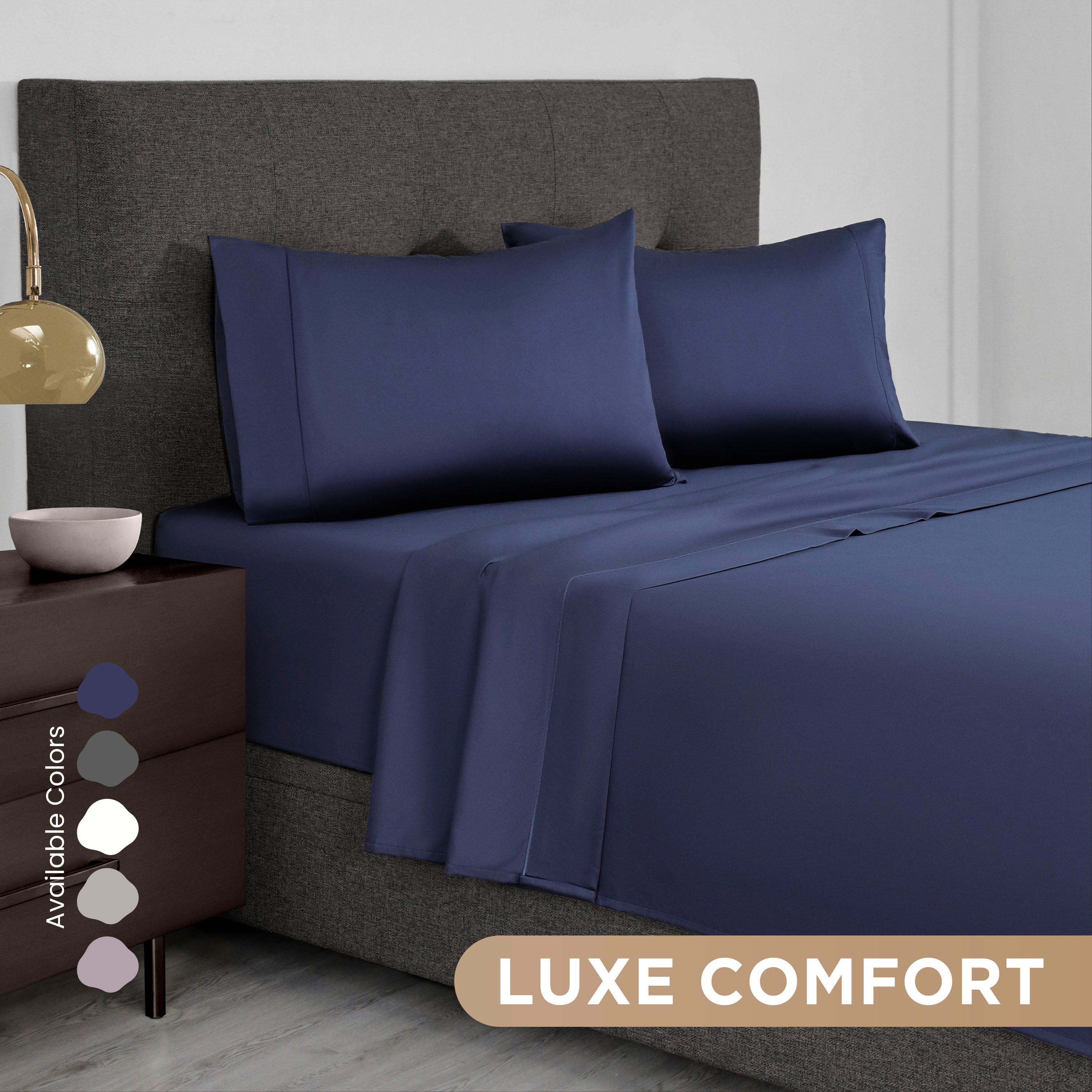 Navy blue Supima cotton sheet set with two pillowcases on a bed, accompanied by a bedside table and lamp.