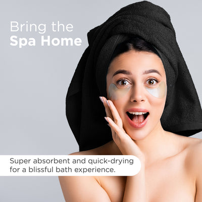 Woman with a towel on her head and under-eye patches, smiling against a gray background.