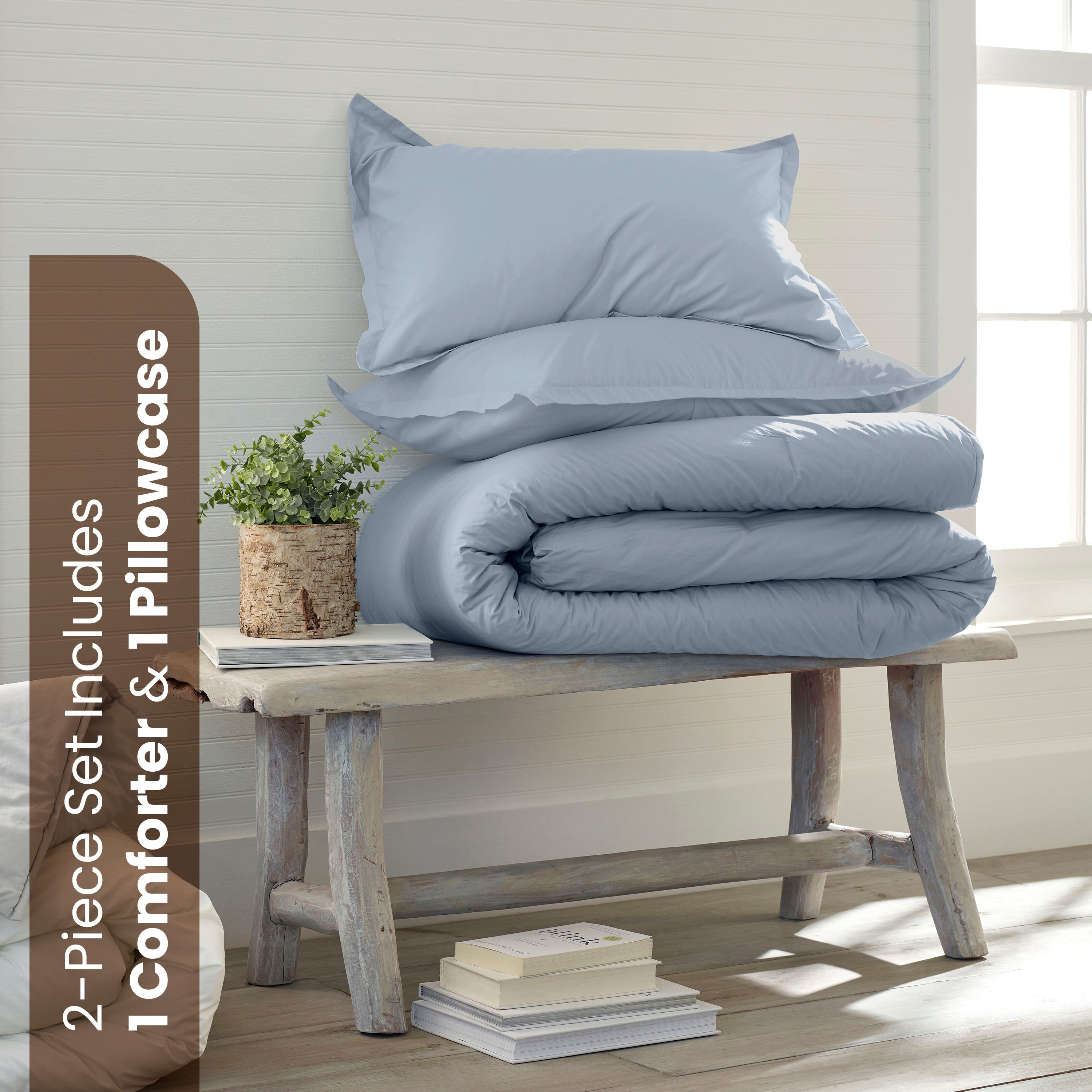Light blue comforter set stacked on a wooden bench with a small plant and books beside it.