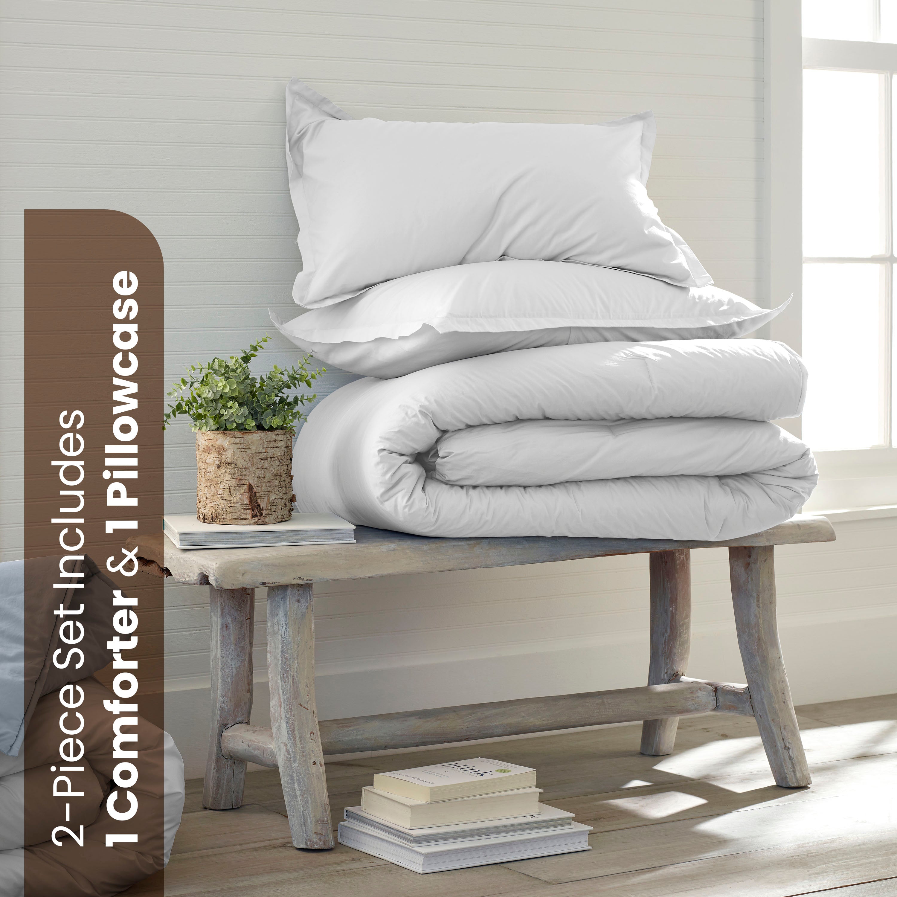 White comforter and pillowcase stacked on a wooden bench with a small plant and books nearby.