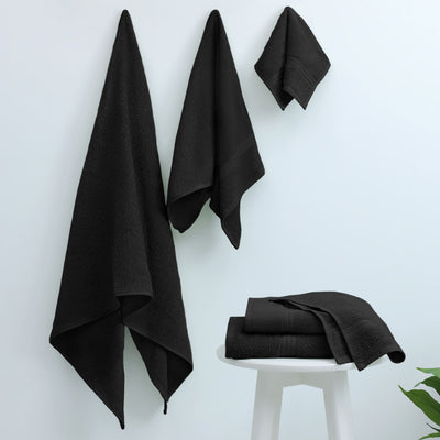 Three black towels hanging on a wall and three folded towels on a white stool.