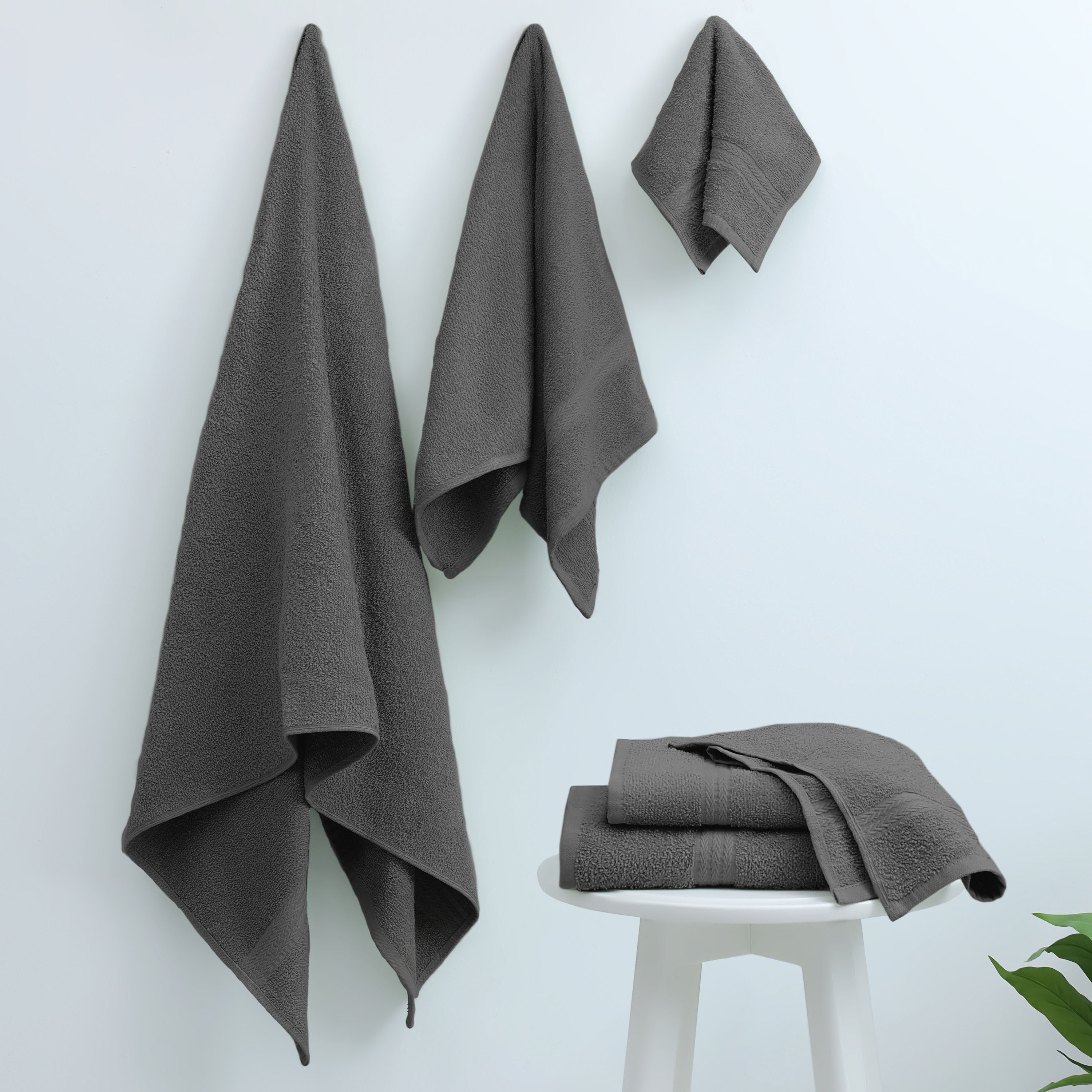 Gray towels hanging on a wall and stacked on a white stool against a light background.