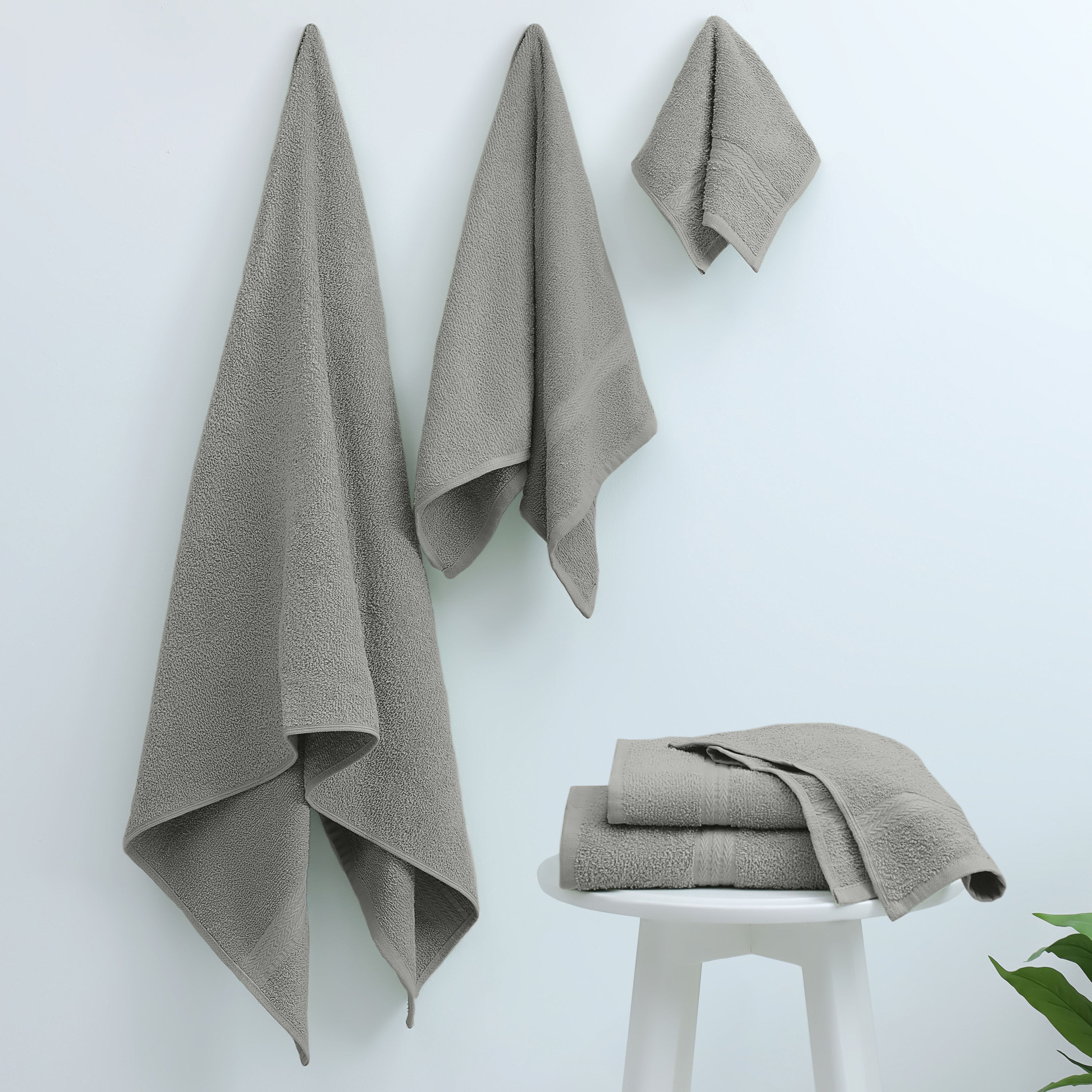 Three gray towels hanging on a wall and three folded towels on a white stool.