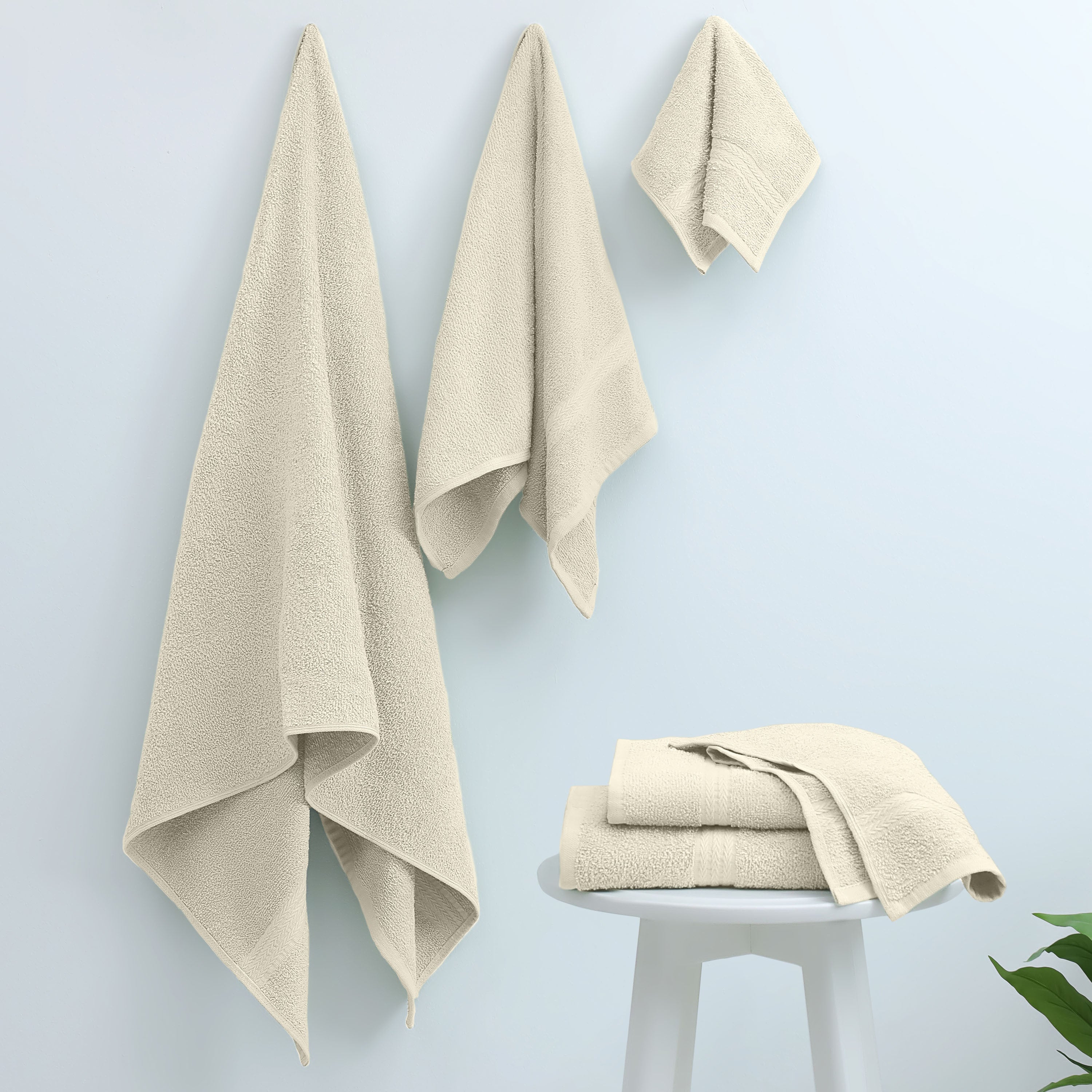 Three beige towels hanging on a wall and two folded towels on a white stool against a light blue background.