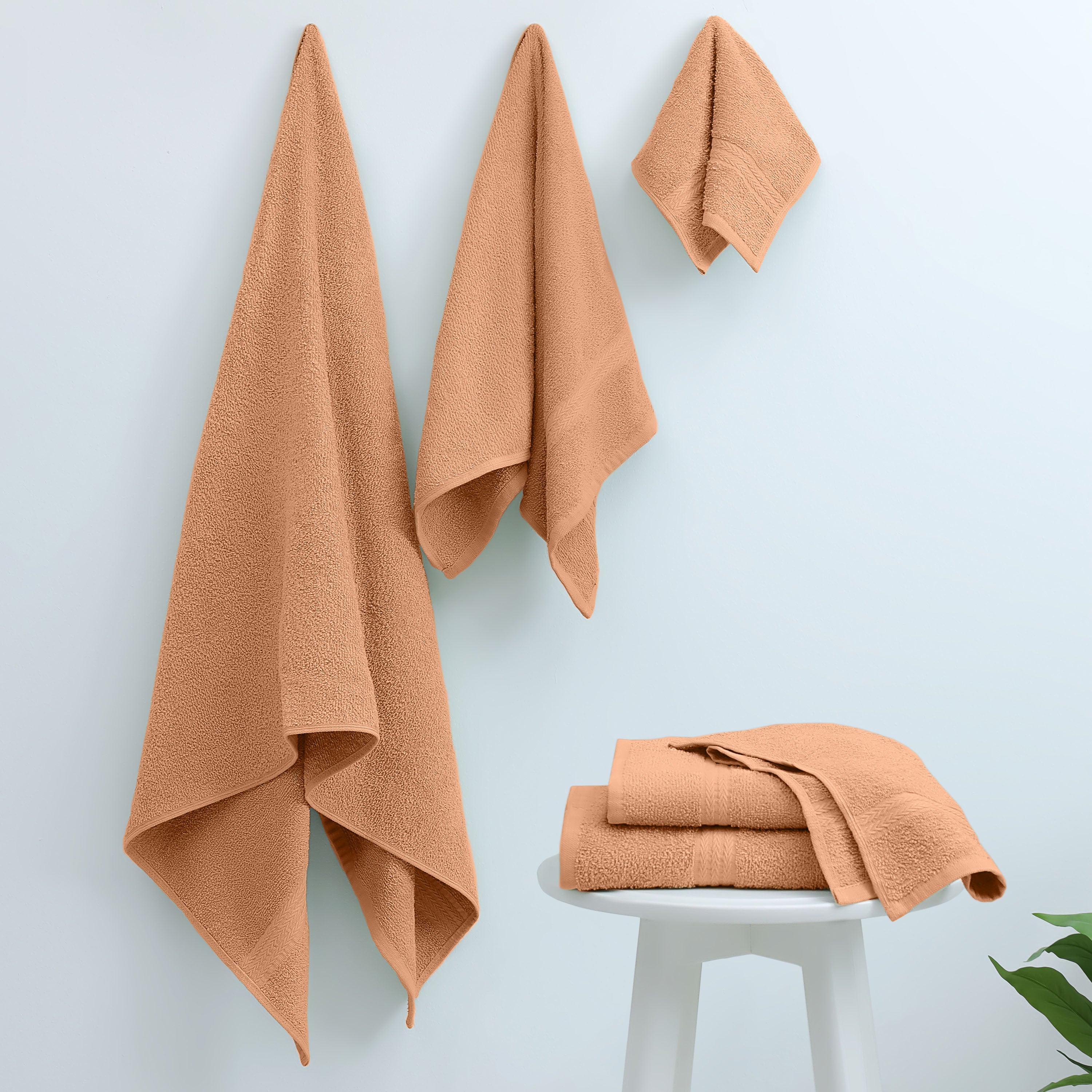 Six peach-colored towels of varying sizes hanging on a wall and resting on a white stool.