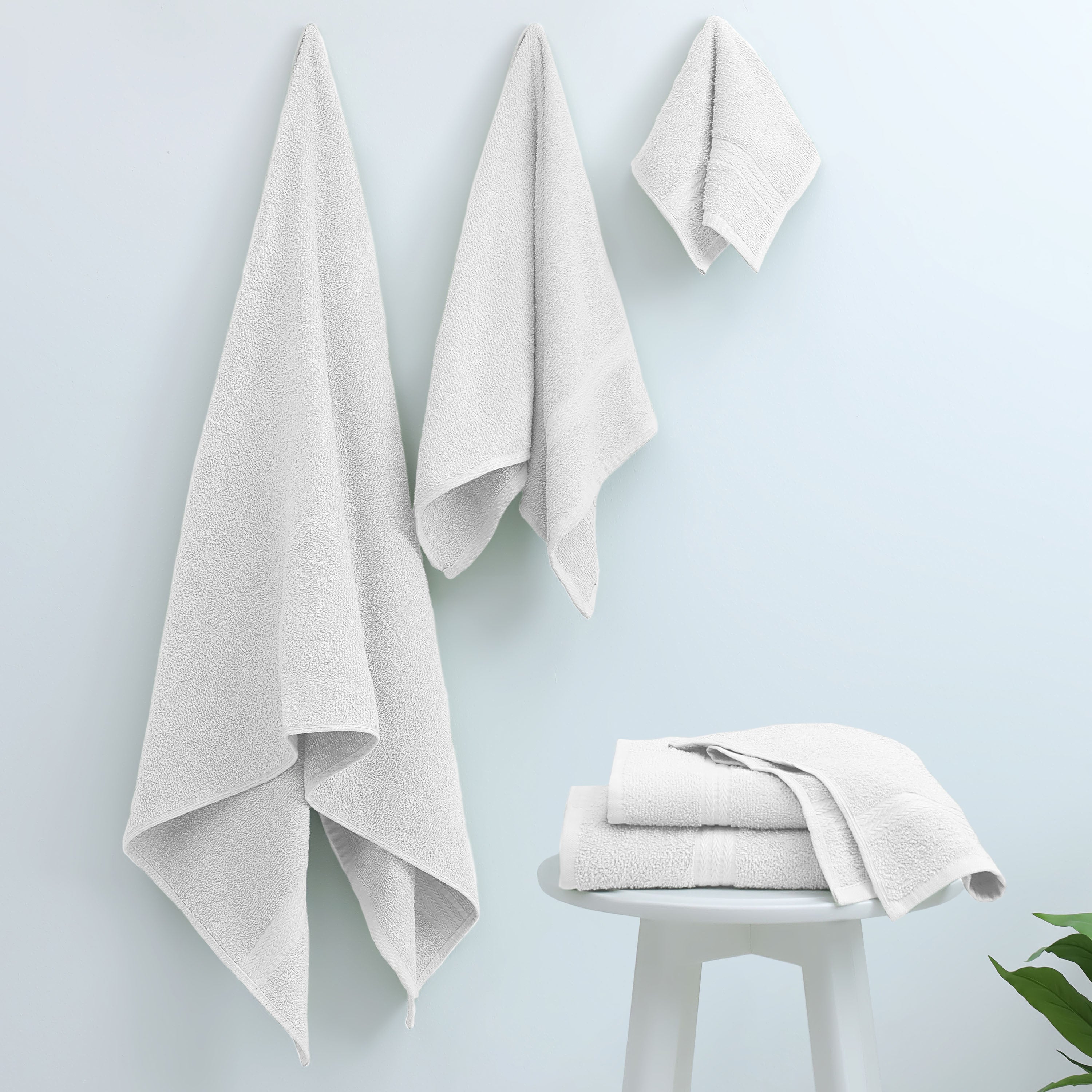 Three white towels hanging on a wall and two folded towels on a small white table.