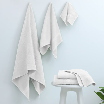 Three white towels hanging on a wall and two folded towels on a small white table.