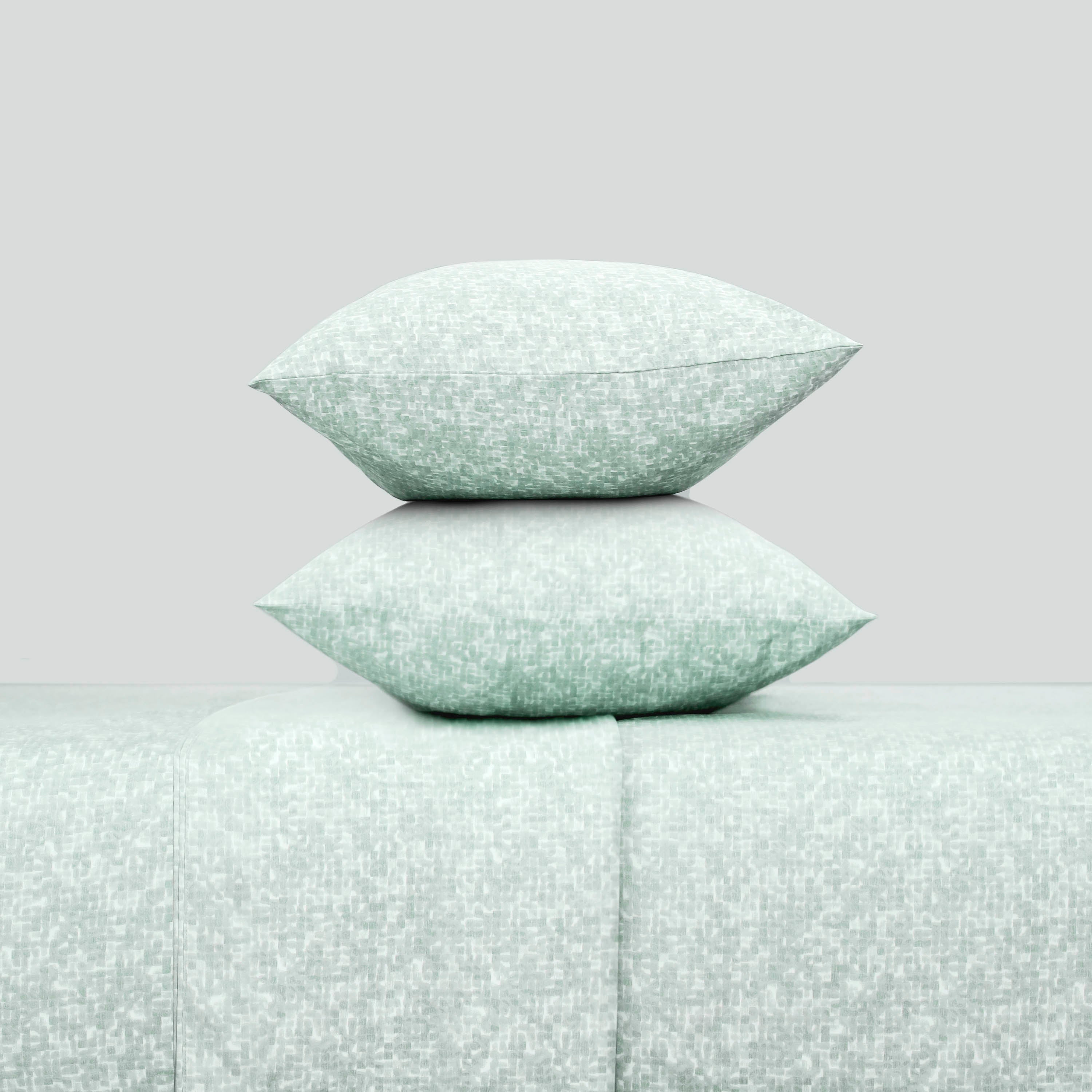 Two decorative pillows in a soft green pattern stacked on a matching sheet set.