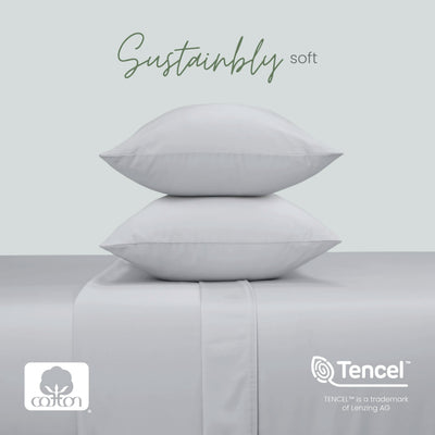 Two grey pillows stacked on a matching upholstered surface, with the words 'Sustainably soft' above. Cotton and Tencel logos appear at the bottom, with a pale gray background.