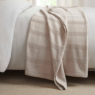 Cotton blanket with a textured design, draped over the edge of a bed.
