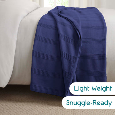 Navy blue cotton blanket draped over a light-colored bedspread with a textured stripe pattern.