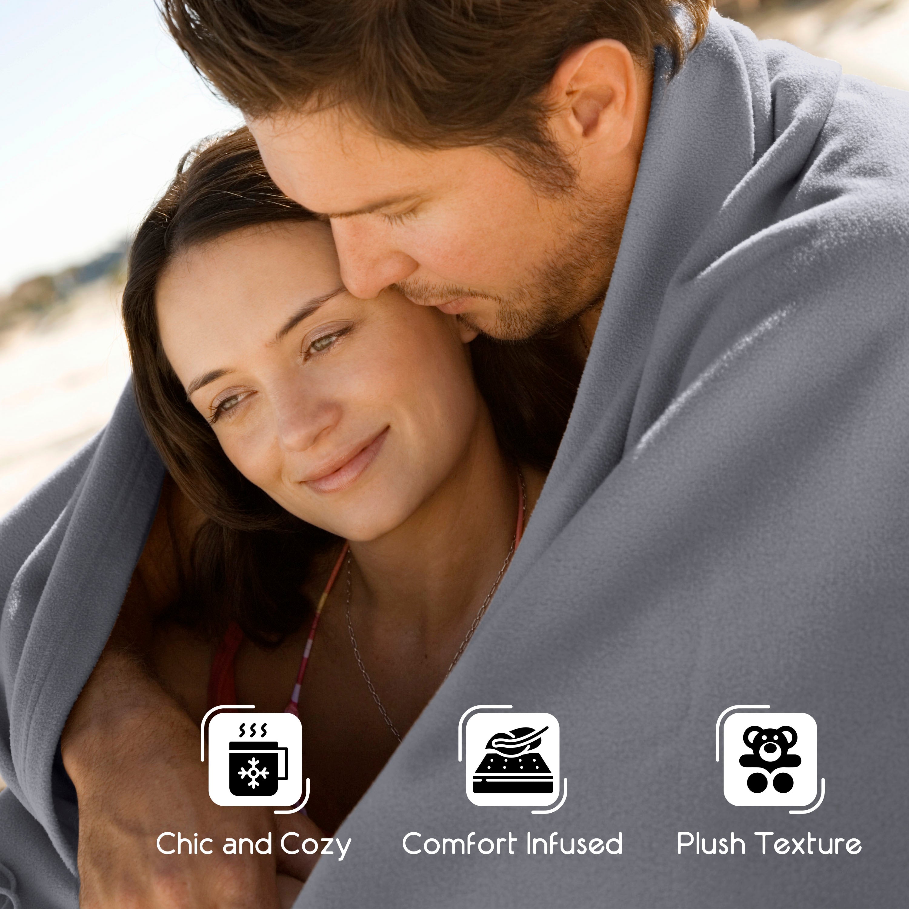 Couple wrapped in a gray blanket, smiling and enjoying each other's company outdoors.