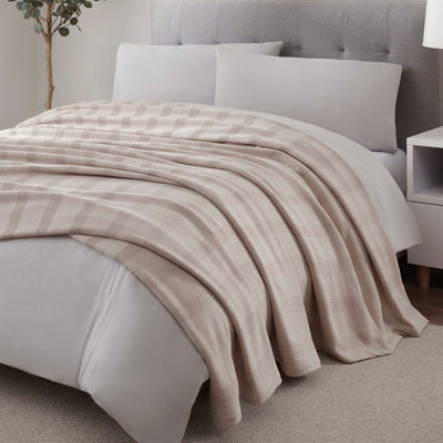 Cotton blanket with a plaid pattern draped over a bed with gray bedding and pillows.