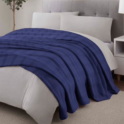 Navy blue cotton blanket draped over a light-colored bedspread with white pillows and a bedside table.