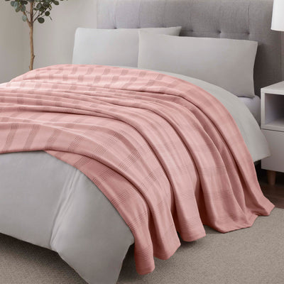 Light pink cotton blanket with a textured plaid pattern draped over a bed with gray bedding and pillows.