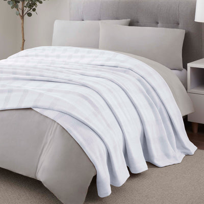 Light blue cotton blanket with a textured plaid pattern draped over a bed with gray bedding and pillows.