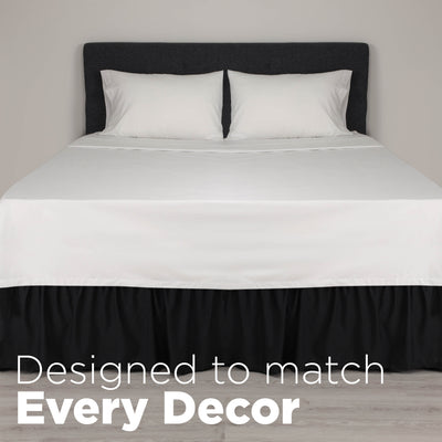 White bedspread with two white pillows and a black ruffled bed skirt on a wooden floor.