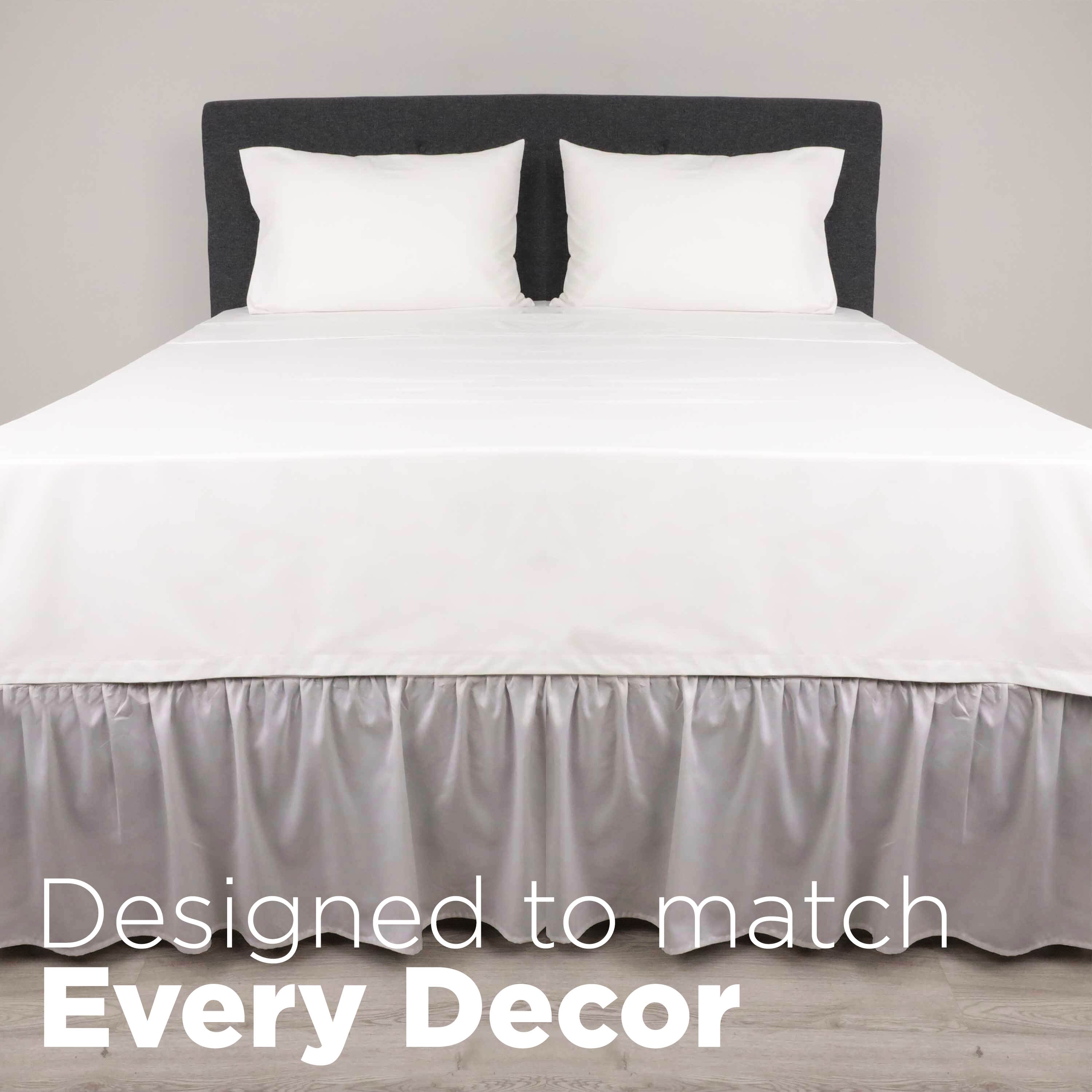 White bed with a ruffled bed skirt and two white pillows against a gray headboard on a light wooden floor.