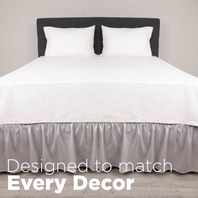 White bed with a ruffled bed skirt and two white pillows against a gray headboard on a light wooden floor.