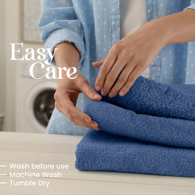 Hands folding blue towels on a table with a washing machine in the background.