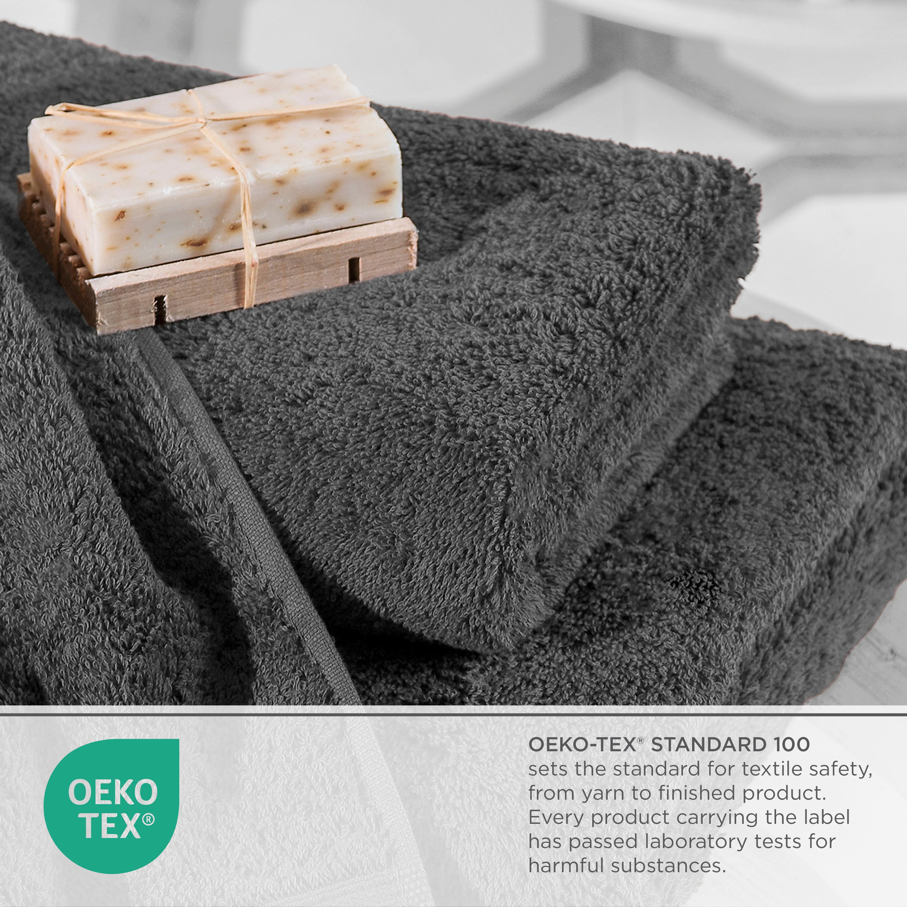 Dark gray towels stacked with a bar of soap on a wooden soap dish, featuring an Oeko-Tex certification label.