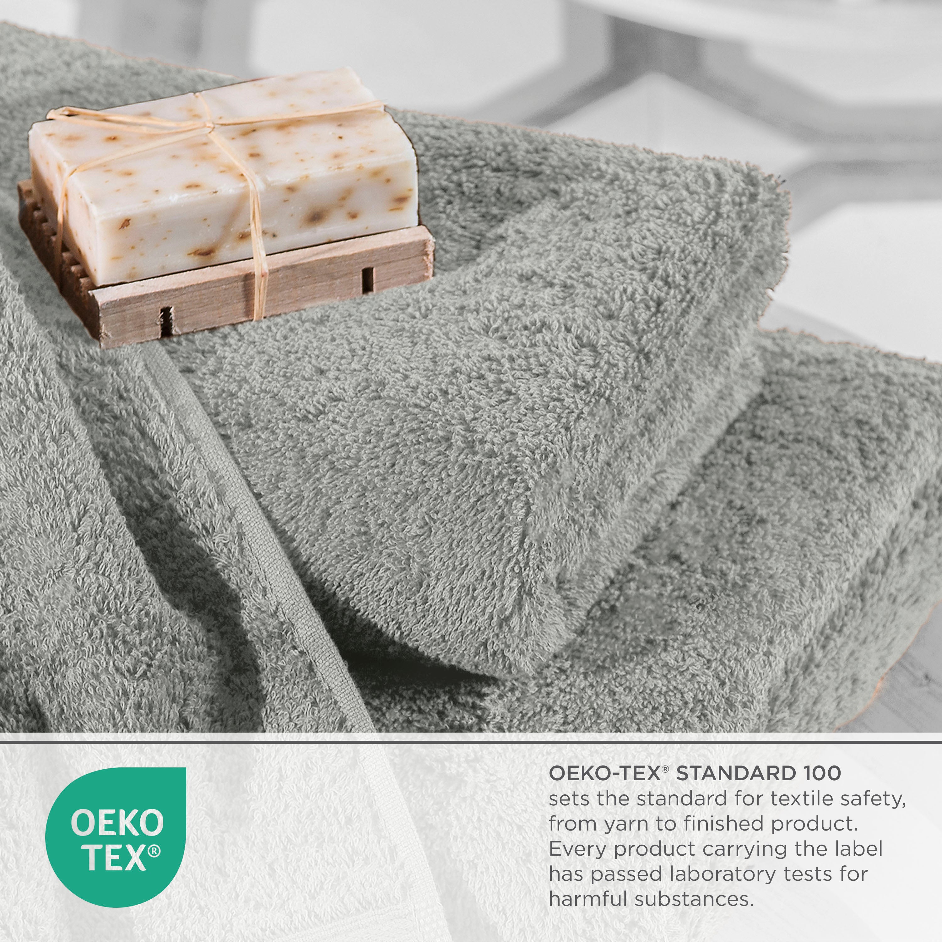 Soft gray towels stacked with a bar of soap on a wooden soap dish, featuring Oeko-Tex certification label.