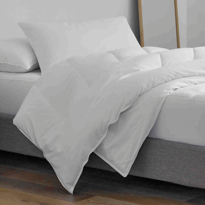 White pillow and pillow protector set placed on a bed with a gray base and wooden floor.