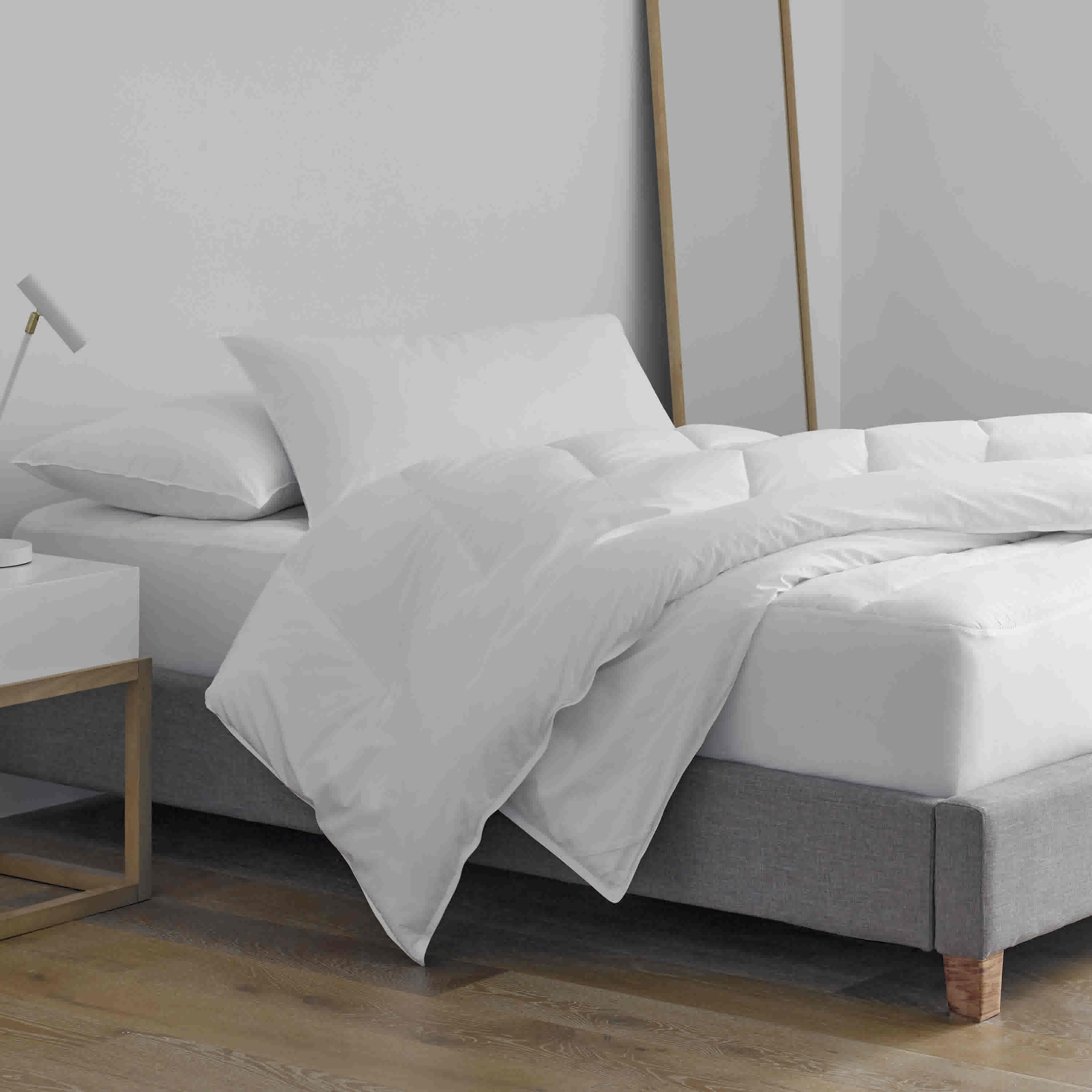 Standard white pillows and a duvet on a bed with a gray upholstered base and a nightstand beside it.