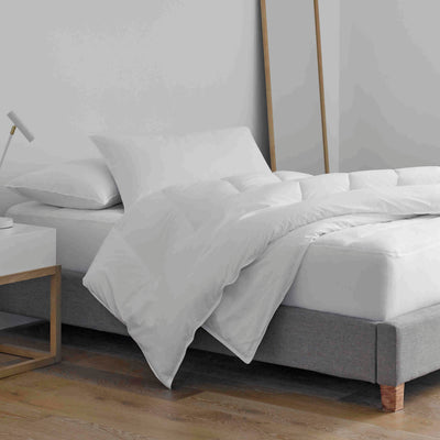 Standard white pillows and a duvet on a bed with a gray upholstered base and a nightstand beside it.