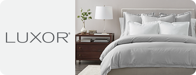 Bedroom scene with Luxor bedding and furniture, featuring a bed with white pillows and gray comforter.