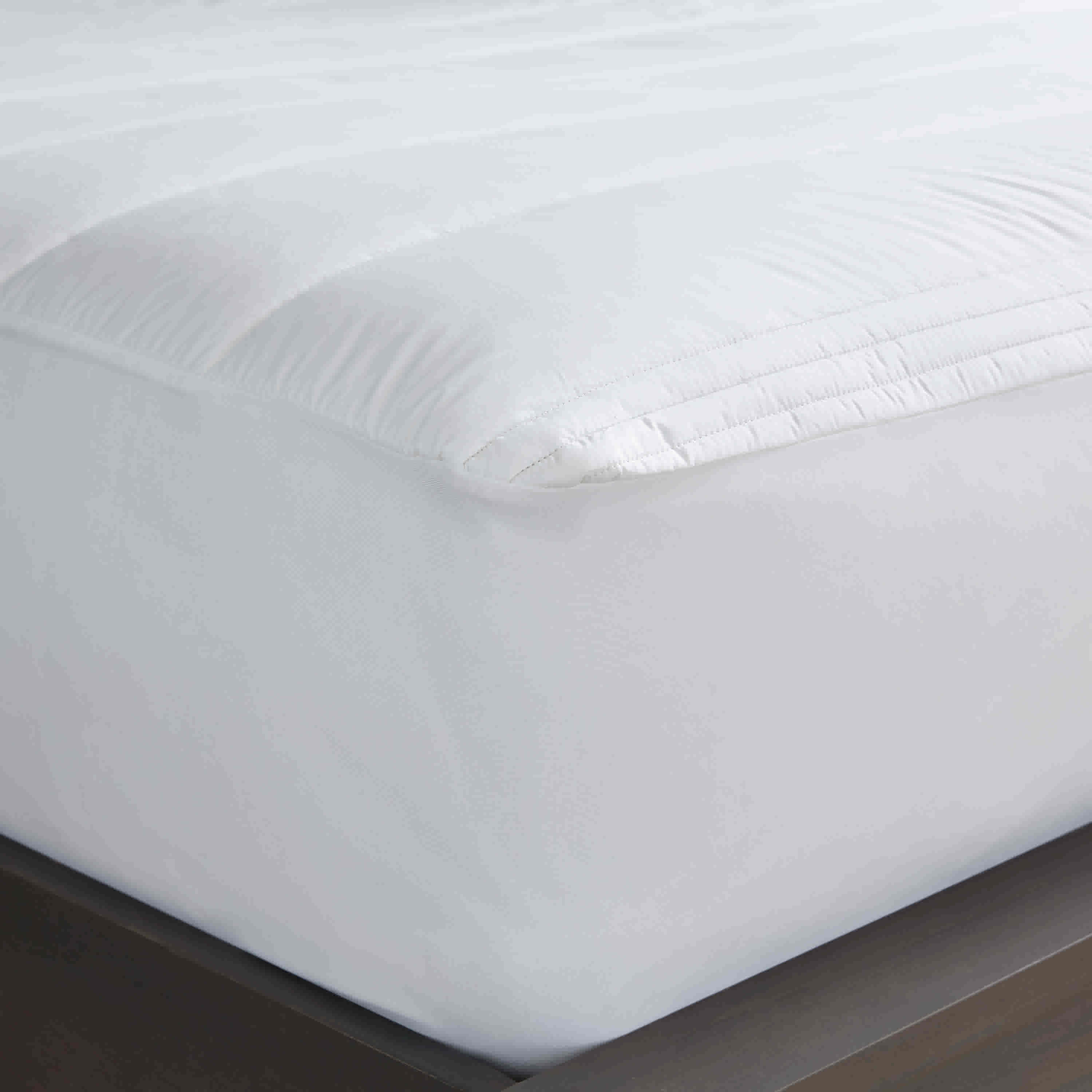 White allergen-barrier mattress pad with a quilted top, fitted to a mattress on a dark wooden bed frame.